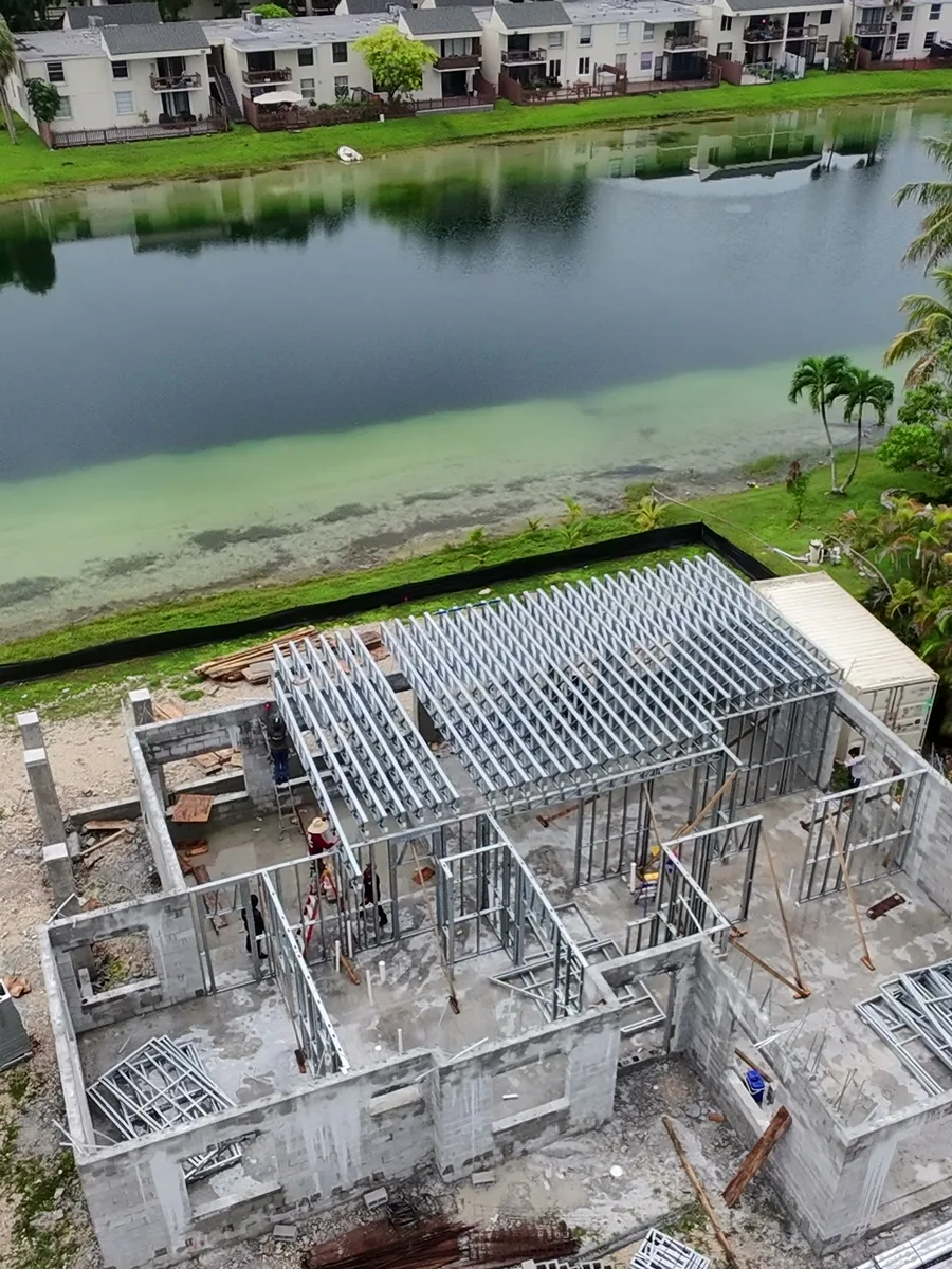 Aerial view of a BuilderK home under construction in Florida, roof trusses set, beside a lake